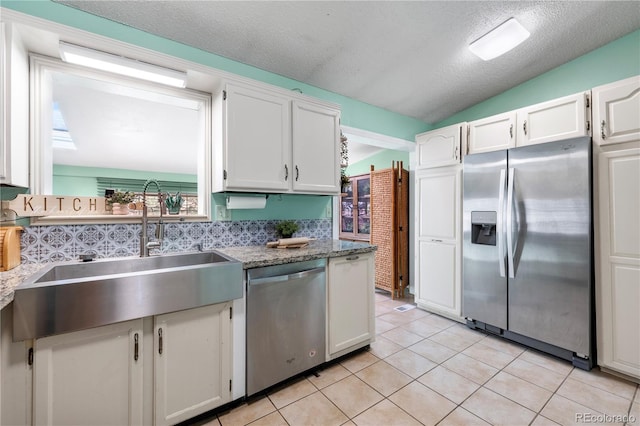 kitchen featuring light tile patterned floors, lofted ceiling, appliances with stainless steel finishes, white cabinets, and a sink