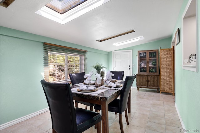 dining room featuring light tile patterned floors, vaulted ceiling with skylight, and baseboards