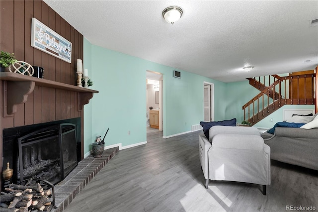 living area featuring a textured ceiling, stairway, a fireplace, and wood finished floors