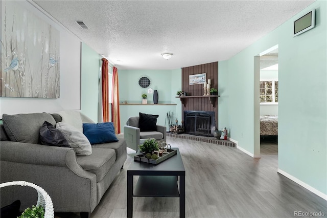 living room featuring a fireplace, visible vents, a textured ceiling, wood finished floors, and baseboards