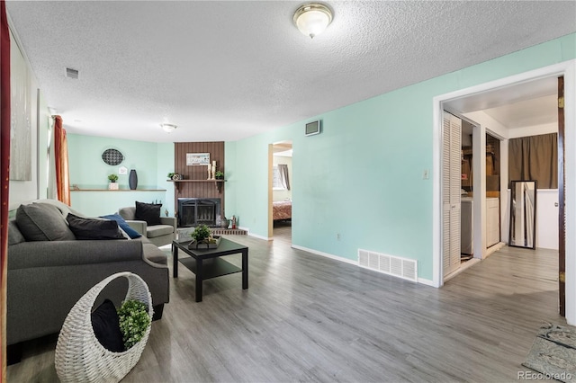 living area featuring visible vents, a fireplace, a textured ceiling, and wood finished floors