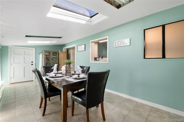 dining space featuring a skylight, light tile patterned floors, and baseboards