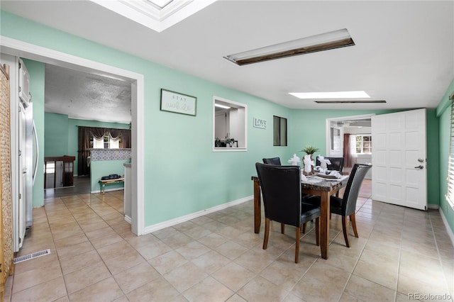 dining area with a skylight, light tile patterned floors, and baseboards