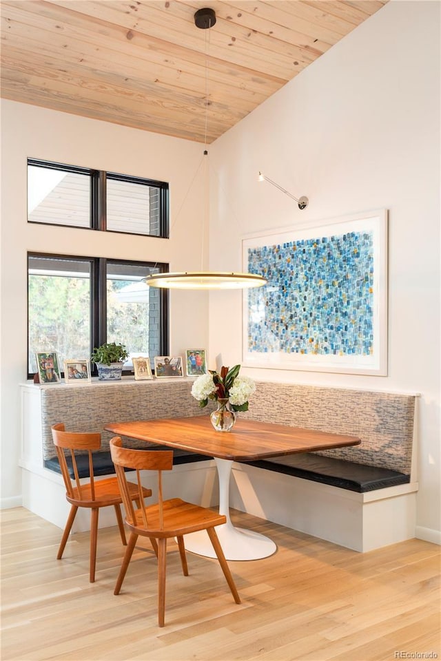 dining area with light wood-type flooring, wooden ceiling, a towering ceiling, and baseboards