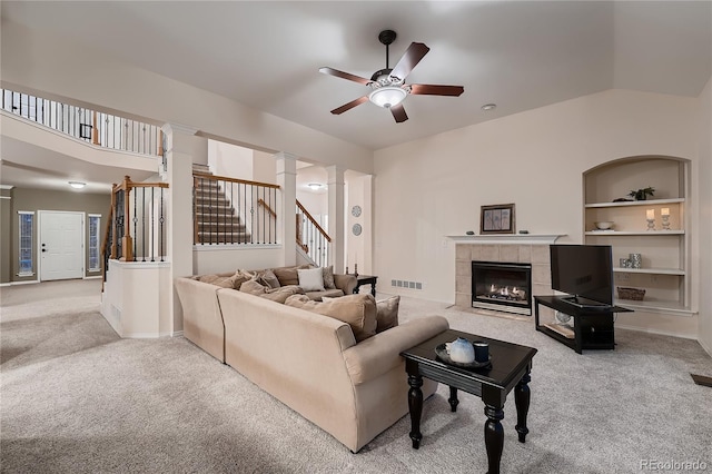 living room with decorative columns, ceiling fan, a tiled fireplace, light colored carpet, and built in features