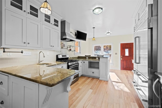 kitchen with sink, wall chimney exhaust hood, stainless steel range with gas cooktop, kitchen peninsula, and pendant lighting