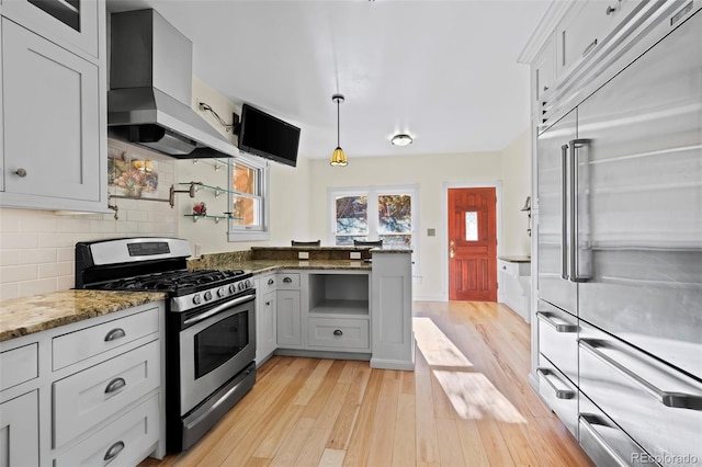 kitchen with stainless steel appliances, extractor fan, decorative light fixtures, light hardwood / wood-style flooring, and dark stone countertops