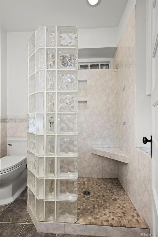 bathroom featuring toilet, tile patterned flooring, tile walls, and tiled shower