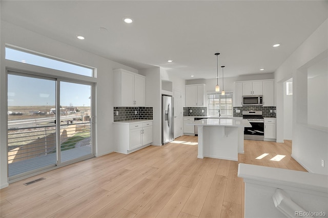 10124 Xanadu St, Commerce City, CO 80022 - kitchen with light wood-style flooring, light countertops, white cabinetry, a kitchen island, and appliances with stainless steel finishes