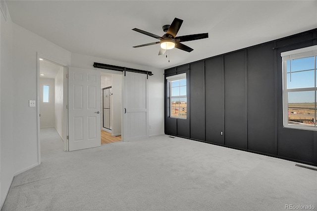 10124 Xanadu St, Commerce City, CO 80022 - unfurnished bedroom with light colored carpet, ceiling fan, visible vents, and a barn door