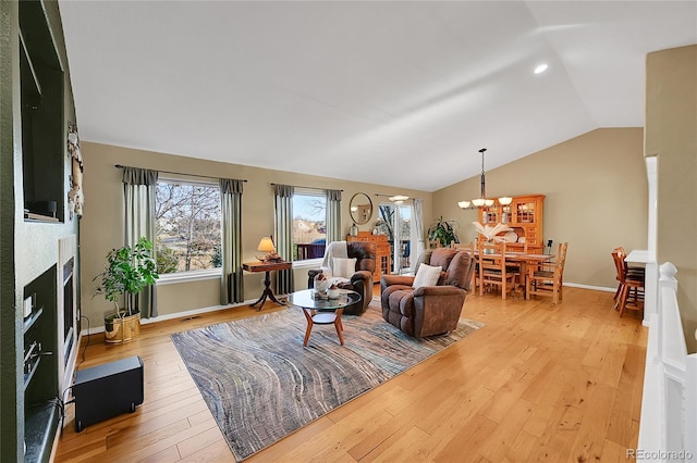 living room featuring light wood-type flooring, a chandelier, a fireplace, and vaulted ceiling