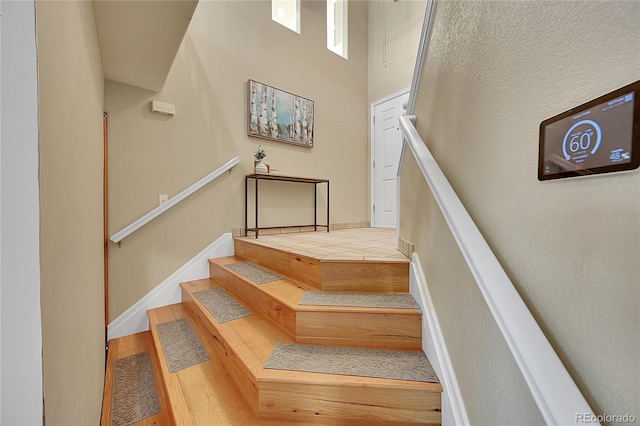 staircase featuring wood finished floors, baseboards, and a towering ceiling