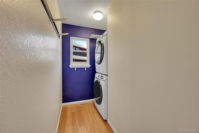 laundry room featuring baseboards, a textured wall, laundry area, stacked washing maching and dryer, and wood finished floors