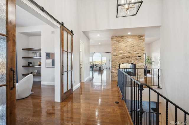 corridor featuring hardwood / wood-style floors, a barn door, a towering ceiling, and an inviting chandelier