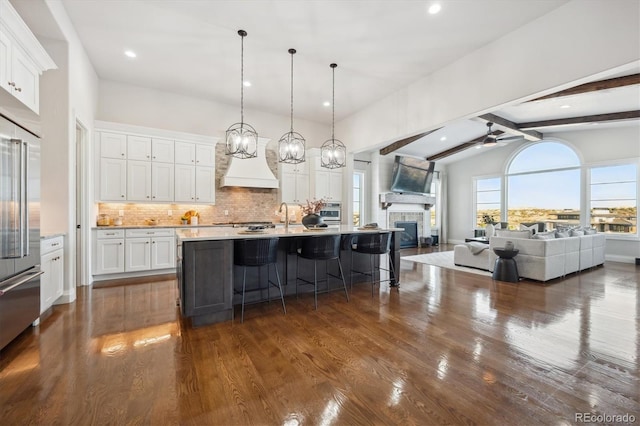 kitchen featuring dark wood-type flooring, pendant lighting, beamed ceiling, white cabinetry, and a tiled fireplace