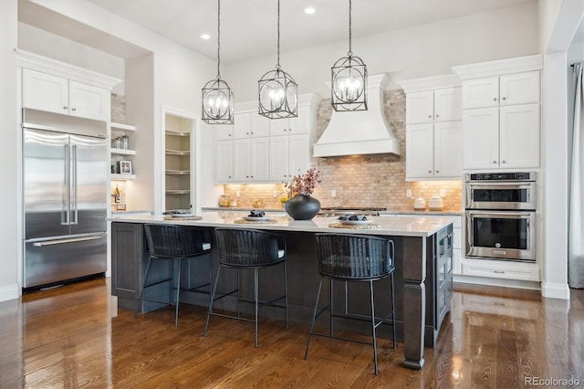 kitchen featuring white cabinets, custom range hood, stainless steel appliances, and an island with sink