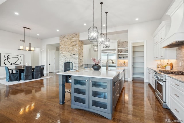 kitchen with premium range hood, stainless steel range, a large island with sink, pendant lighting, and white cabinets