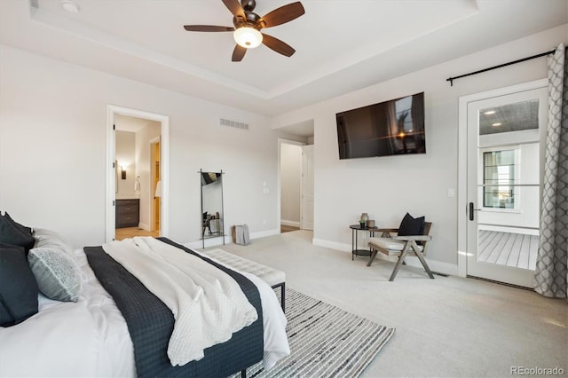 bedroom with connected bathroom, light colored carpet, a raised ceiling, and ceiling fan