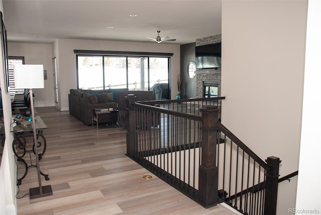 staircase featuring a stone fireplace, ceiling fan, and hardwood / wood-style floors