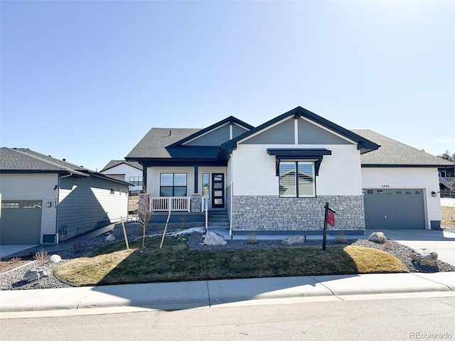 view of front of house with an attached garage, covered porch, driveway, stone siding, and roof with shingles