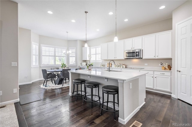 26722 E Peakview Pl, Aurora, CO 80016 - kitchen featuring stainless steel microwave, an island with sink, a breakfast bar area, a chandelier, and dark wood finished floors