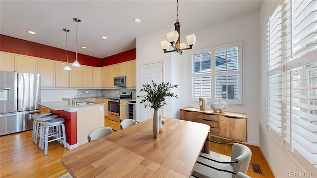 6187 Reed Way, Arvada, CO 80003 - kitchen with appliances with stainless steel finishes, light wood-style floors, a center island with sink, light countertops, and a chandelier