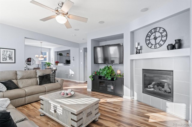 living room with ceiling fan with notable chandelier, light hardwood / wood-style flooring, and a fireplace