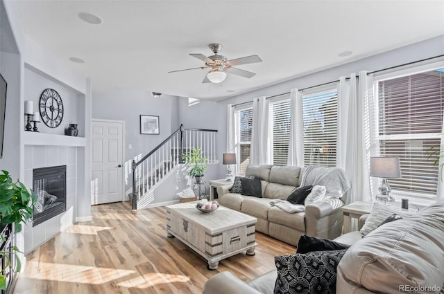 living room with a tile fireplace, light wood-type flooring, and ceiling fan