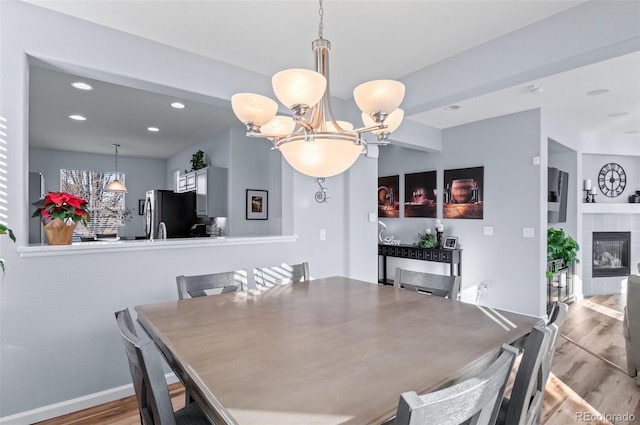 dining area with a tile fireplace, an inviting chandelier, and light hardwood / wood-style flooring