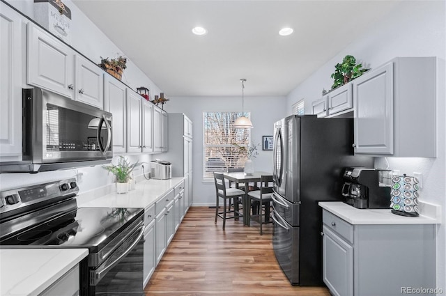 kitchen with appliances with stainless steel finishes, pendant lighting, and hardwood / wood-style floors