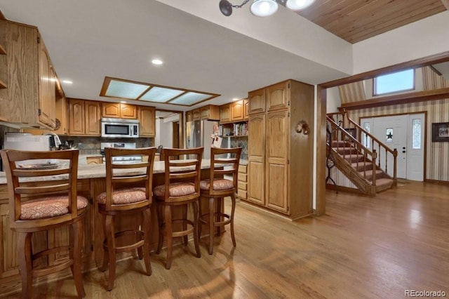 60 N County Highway 67, Sedalia, CO 80135 - kitchen with appliances with stainless steel finishes, a peninsula, light wood-style floors, a breakfast bar, and brown cabinetry