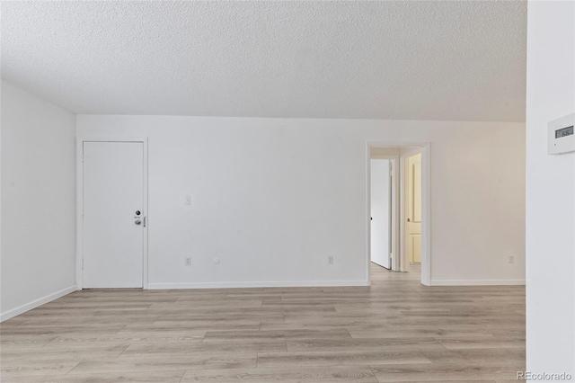 empty room with light wood-style floors, baseboards, and a textured ceiling