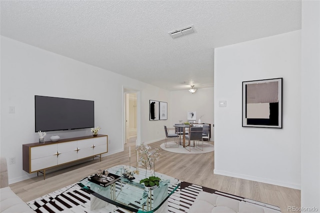 living area with visible vents, baseboards, a textured ceiling, and light wood finished floors