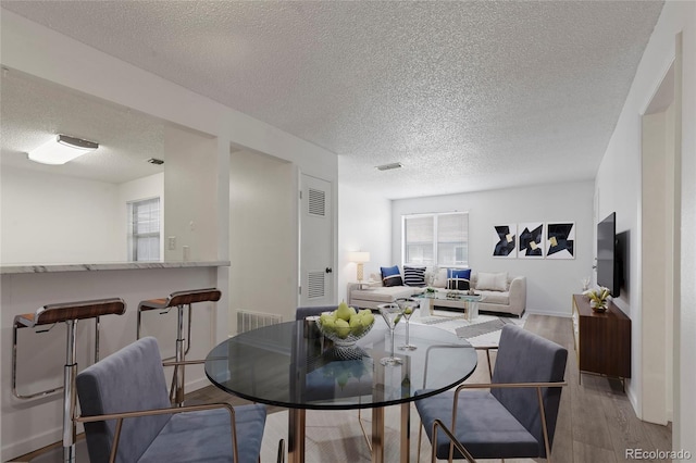 dining area with visible vents, baseboards, a textured ceiling, and wood finished floors