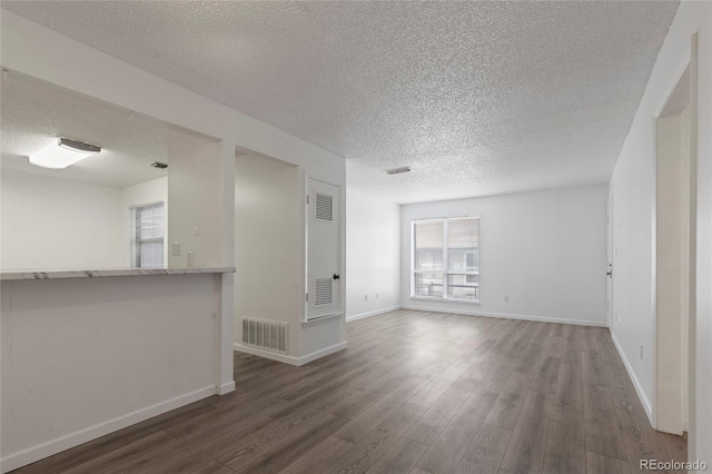 empty room with visible vents, a textured ceiling, baseboards, and wood finished floors