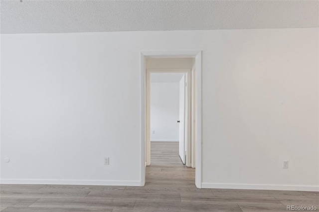 unfurnished room with a textured ceiling, baseboards, and wood finished floors