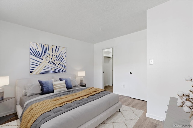 bedroom featuring a spacious closet, a textured ceiling, light wood-type flooring, and baseboards