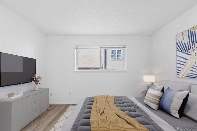 bedroom with light wood finished floors, a textured ceiling, and baseboards