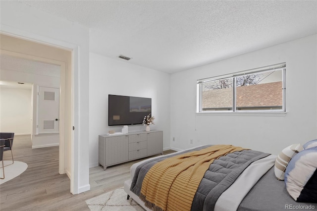 bedroom featuring baseboards, visible vents, light wood-type flooring, and a textured ceiling