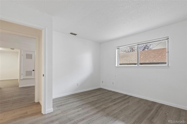 spare room with visible vents, a textured ceiling, baseboards, and wood finished floors