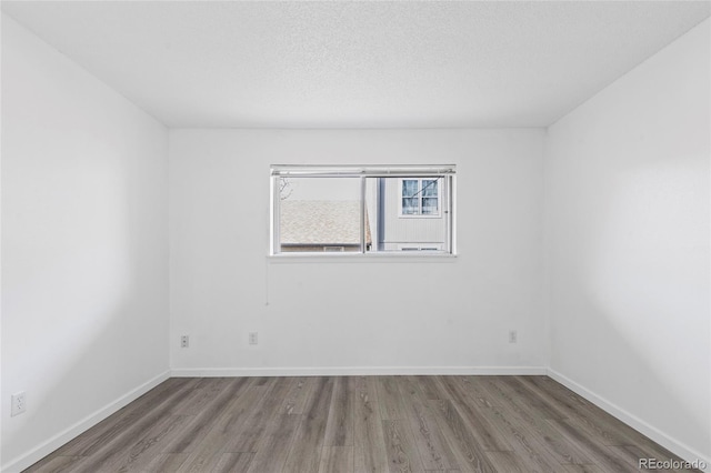 unfurnished room featuring a textured ceiling, baseboards, and wood finished floors