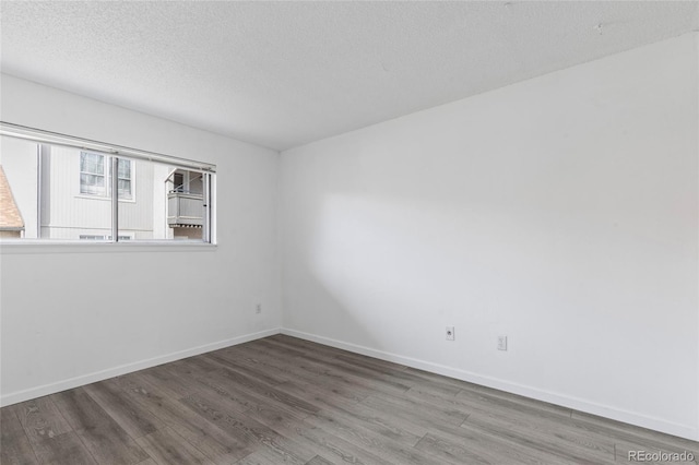 unfurnished room with a textured ceiling, baseboards, and wood finished floors