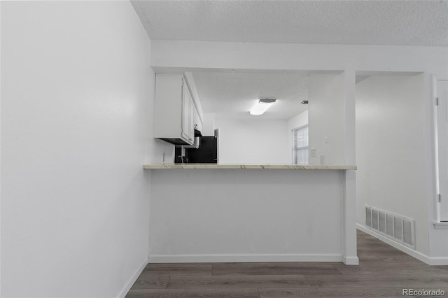 7185 S Gaylord St Unit G13, Littleton, CO 80122 - kitchen with a textured ceiling, baseboards, dark wood finished floors, white cabinetry, and a peninsula