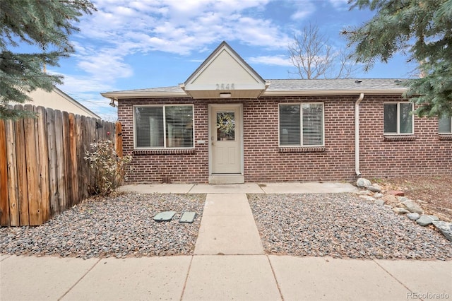 view of front of house with brick siding, roof with shingles, and fence