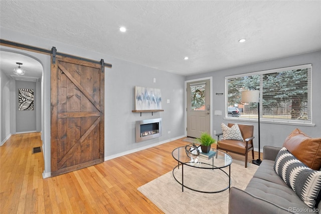 living room featuring visible vents, hardwood / wood-style flooring, a textured ceiling, a barn door, and baseboards