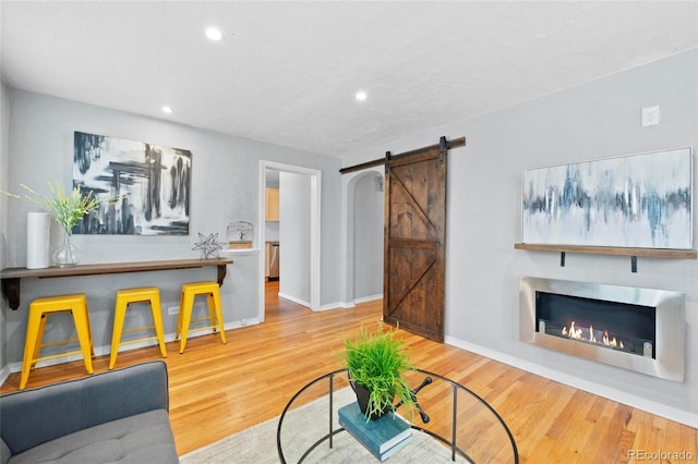 living room with baseboards, a barn door, recessed lighting, wood finished floors, and a glass covered fireplace