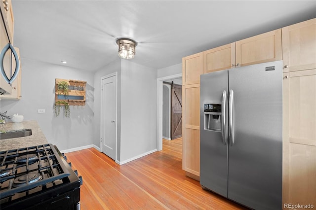 kitchen featuring light wood-type flooring, light brown cabinets, a sink, stainless steel fridge, and baseboards