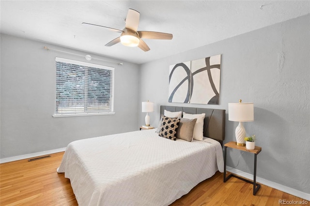 bedroom with ceiling fan, visible vents, baseboards, and wood finished floors