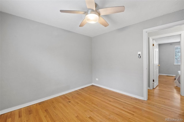 spare room with baseboards, light wood-style floors, and a ceiling fan