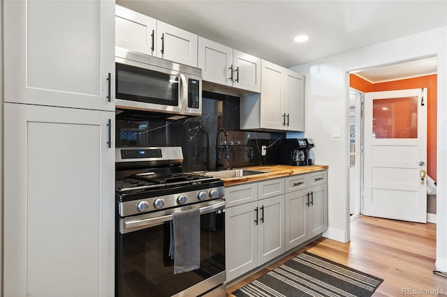 kitchen with light wood finished floors, tasteful backsplash, wood counters, appliances with stainless steel finishes, and a sink